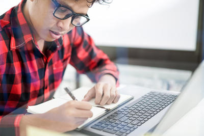 Young man wearing a red plaid shirt and glasses, taking a comprehensive psychological test on a laptop in a well-lit environment.