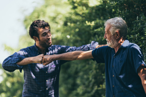 A young man and an older man engage in a playful fist bump outdoors that symbolize bond through psychotherapy for all ages