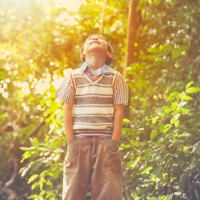 Happy asian boy looking up at forest, travel on vacation. Cute child relaxing outdoors in the day time with bright sunlight. Positive human emotion.