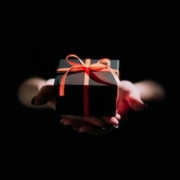 Hands holding a gift out of darkness, representing gift-giving as an act of kindness to soothe anxiety and restore connection.