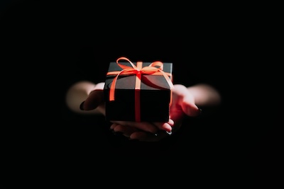 Hands holding a gift out of darkness, representing gift-giving as an act of kindness to soothe anxiety and restore connection.