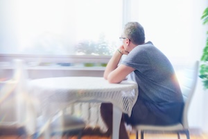 A man experiencing Prolonged Grief Disorder sitting by a window