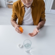 An older man holding psychiatric medications next to a glass of water, reflecting on evidence-based mental health treatment.