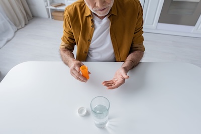 An older man holding psychiatric medications next to a glass of water, reflecting on evidence-based mental health treatment.
